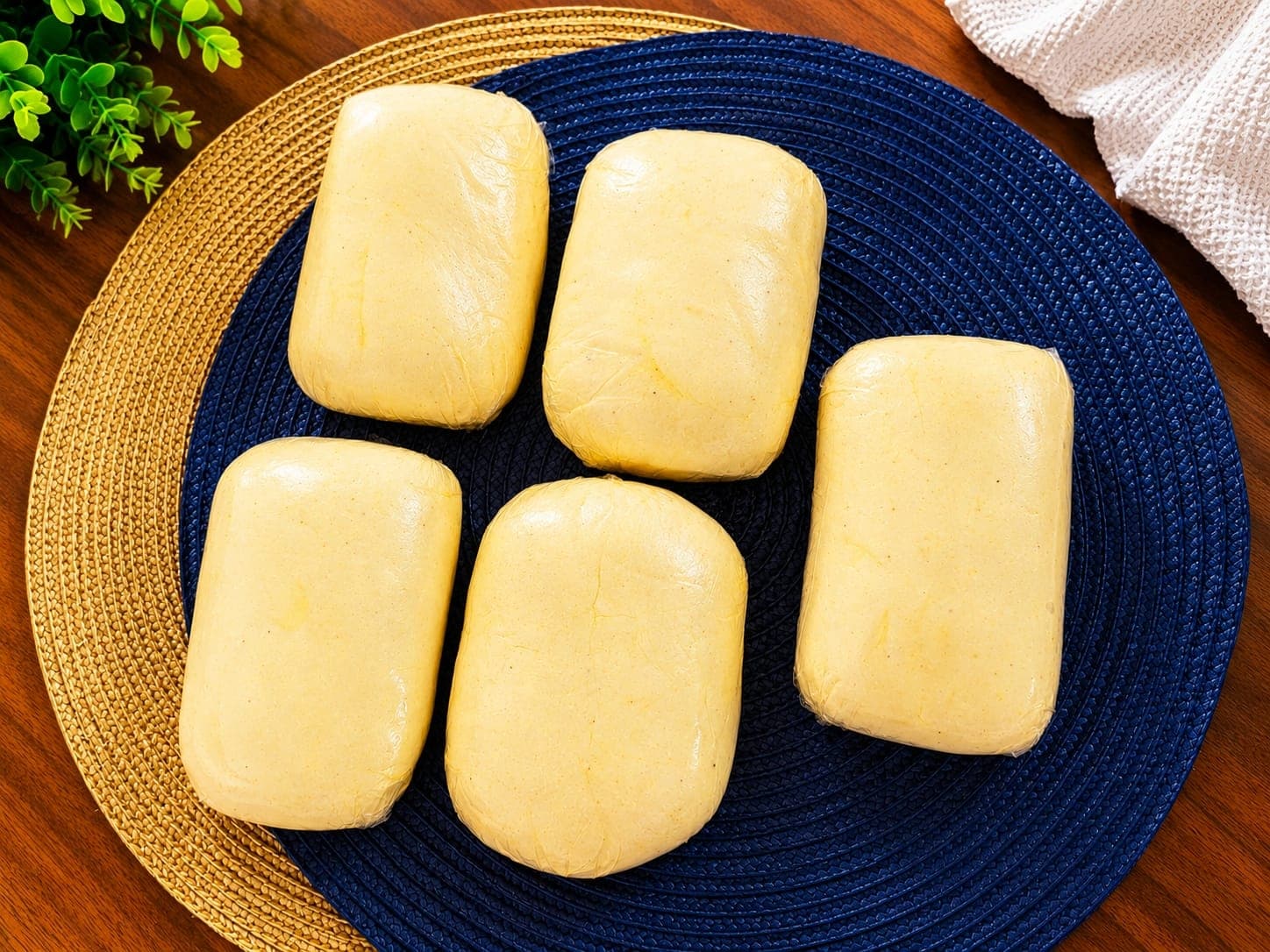 Cinco porciones de masa de pandebono sobre individuales azul y dorado